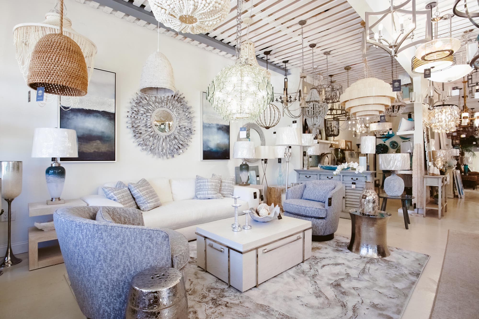 Rows of chandeliers and pendant lights in glass and brass, hanging from a wood-slat ceiling in the Venice Home & Lighting showroom